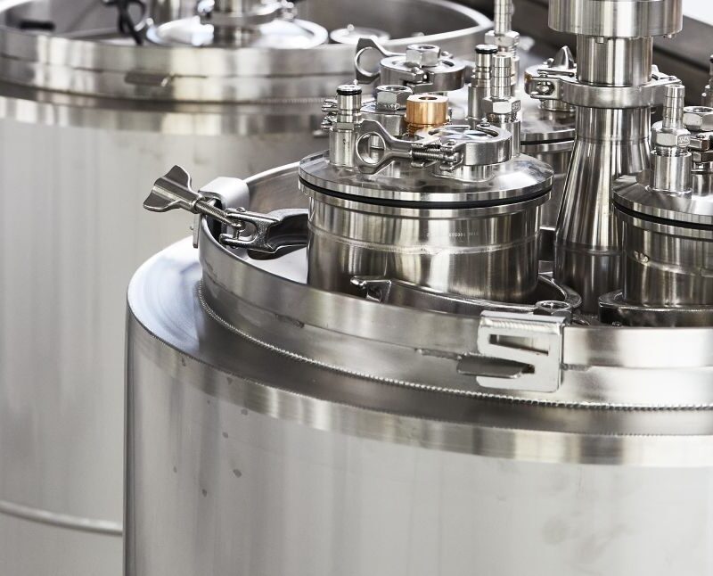 Large stainless steel bioreactors or industrial fermentation tanks with various valves and pipes, situated in a clean, modern laboratory or manufacturing facility.