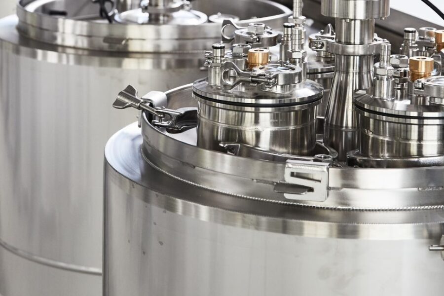 Large stainless steel bioreactors or industrial fermentation tanks with various valves and pipes, situated in a clean, modern laboratory or manufacturing facility.